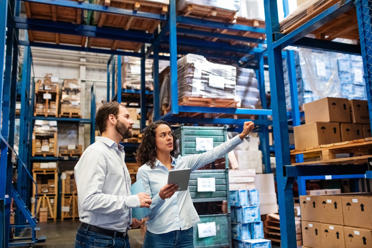 Two workers in a warehouse pointing at the shelves. The female worker is holding a tablet.