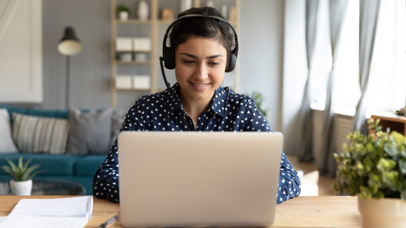 Woman with headphones on working at home on a laptop at a desk.