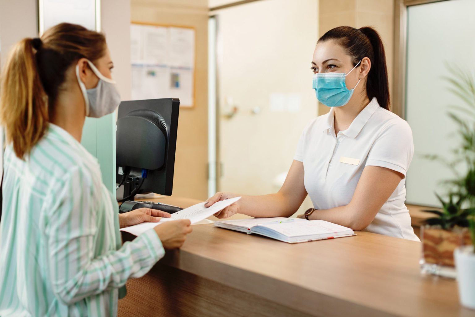 Medical Assistant wearing a mask and handing out a paper to a coworker who is also wearing a mask.